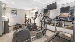 A modern fitness center with cardio machines, weightlifting equipment, and a large mirror. - Keene Elm City Hotel, an Ascend Collection Hotel (Keene)