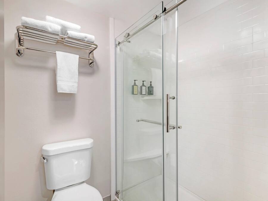 Un baño con inodoro, ducha con mampara de vidrio, toallero con varias toallas y estante con artículos de aseo.