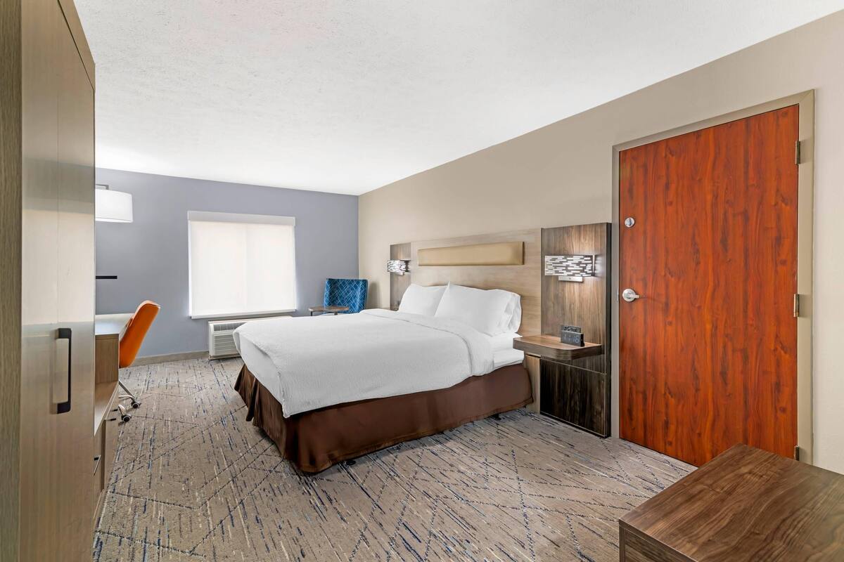 Een hotelkamer met een bed, een bureau, een stoel, een houten deur en een raam.
