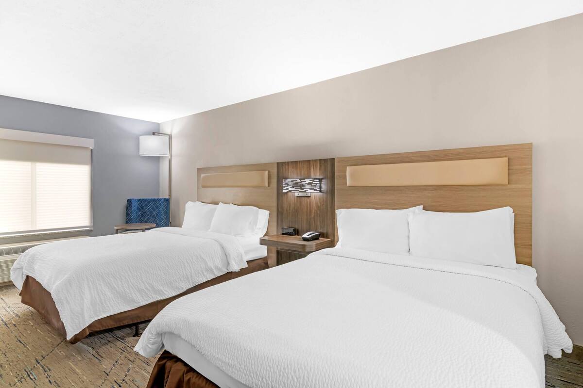 Een hotelkamer met twee bedden, een nachtkastje met een lamp en een kunstwerk aan de muur.