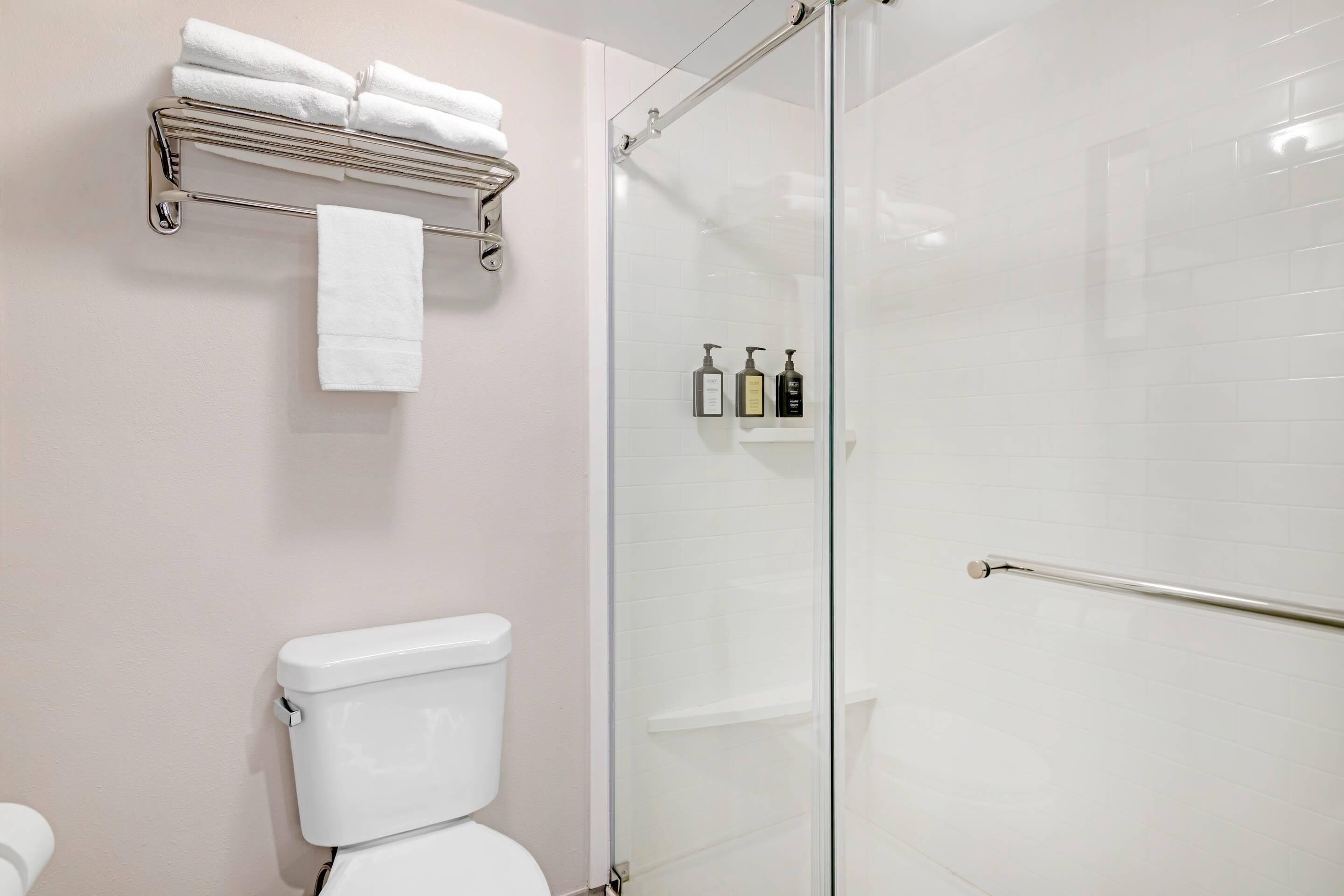 Ein Badezimmer mit einer gläsernen Duschkabine, einer Toilette und einem Handtuchhalter mit gefalteten Handtüchern.