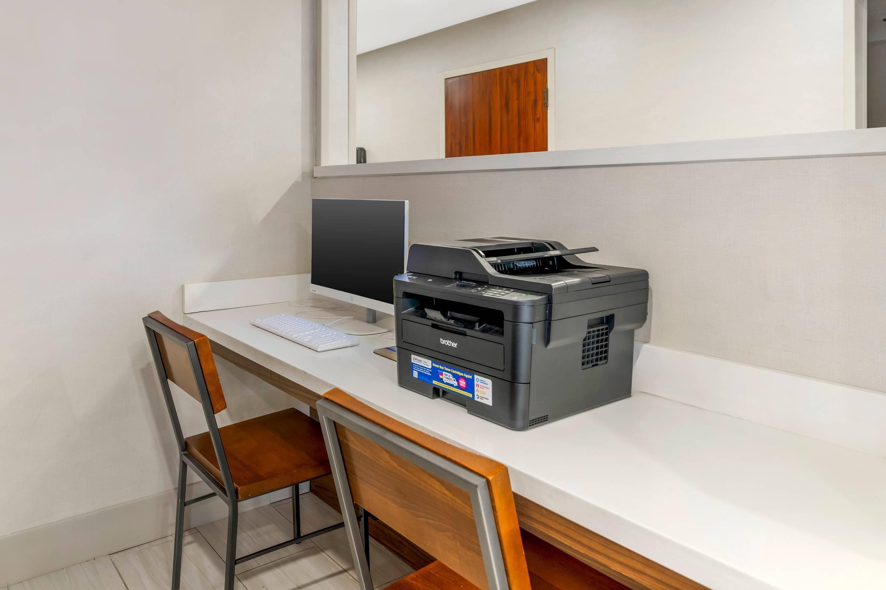 A desk with a computer, a Brother printer, and a wooden chair.