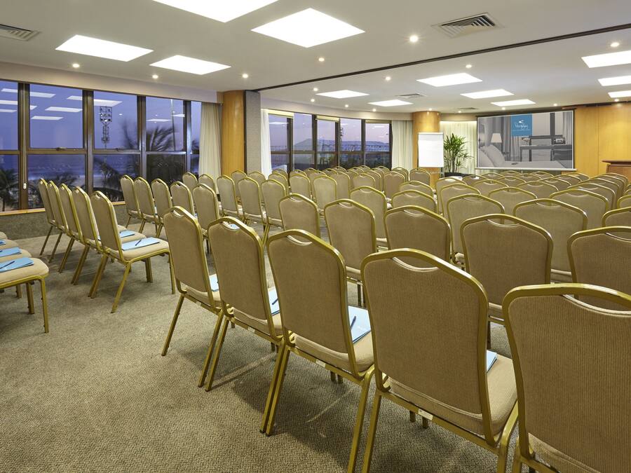 Ein Konferenzraum mit Reihen von Stühlen, großen Fenstern und Deckenleuchten.
