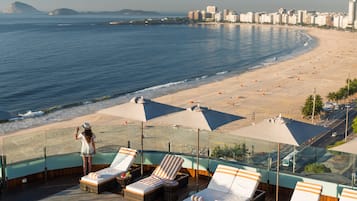 A rooftop pool area with lounge chairs and umbrellas overlooking a beach.