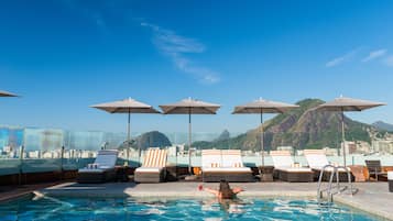 Una piscina al aire libre, sombrillas, sillones reclinables de piscina