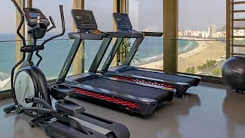 A gym with cardio machines and a view of the beach.