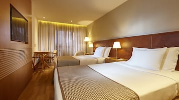 Quarto de hotel com duas camas, soalho de madeira, escrivaninha com cadeira e uma janela grande com cortinas.