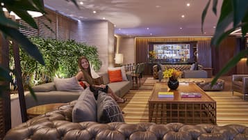 A modern lounge area with leather sofas, a bar, and a variety of plants.