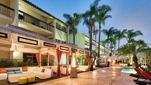 A hotel courtyard with outdoor seating, a pool, and palm trees. - Atrium Hotel at Orange County Airport (Irvine)