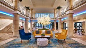 A spacious lobby with a central seating area, a staircase, and a large window. - Atrium Hotel at Orange County Airport (Irvine)