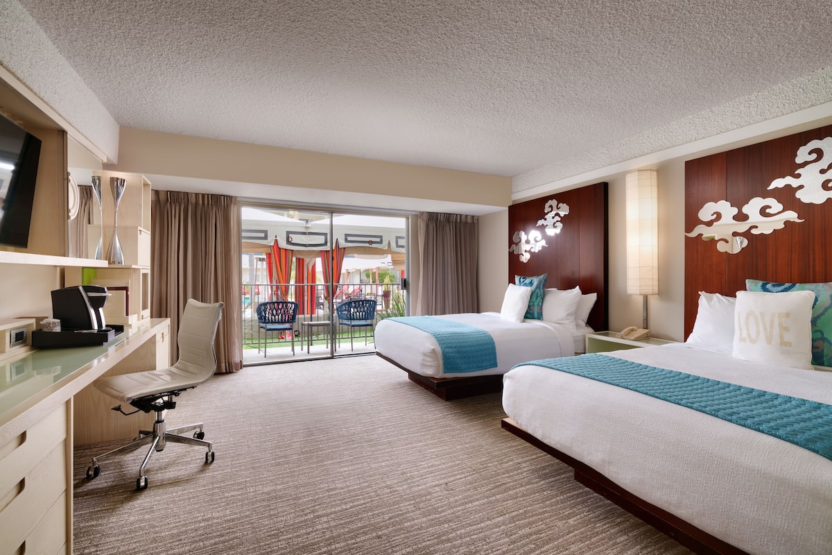 A hotel room with two beds, a desk, a chair, and a TV.