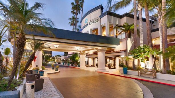 A hotel entrance with a covered walkway, palm trees, and outdoor seating. - Atrium Hotel at Orange County Airport (Irvine)