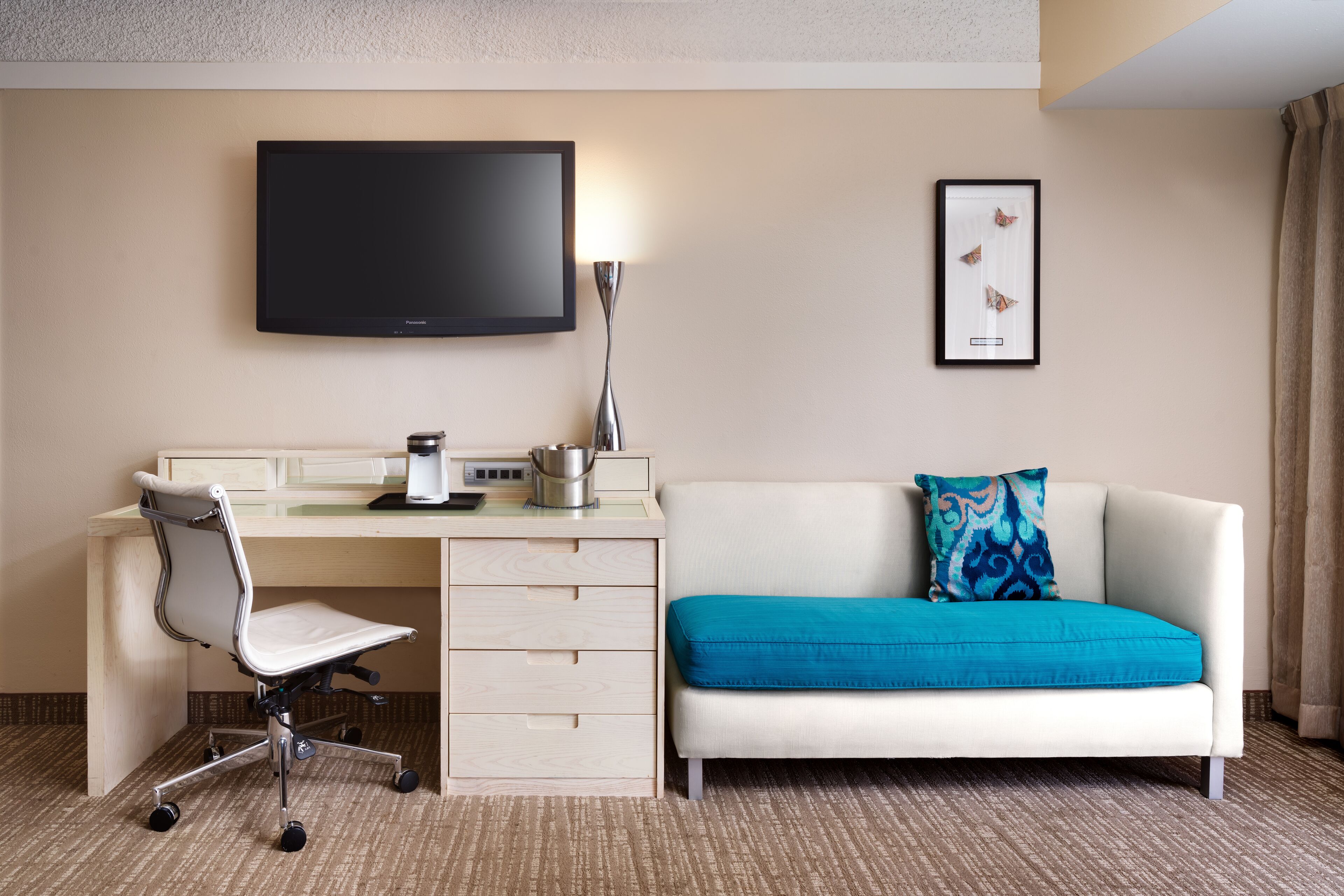 Una camera d'albergo con un letto, una scrivania, una sedia, una TV a schermo piatto, una lampada e un quadro appeso al muro.