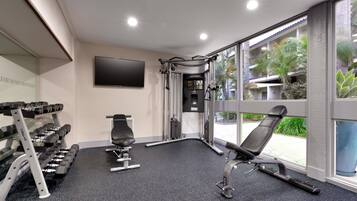 A gym with exercise equipment, a TV, and large windows overlooking a building.
