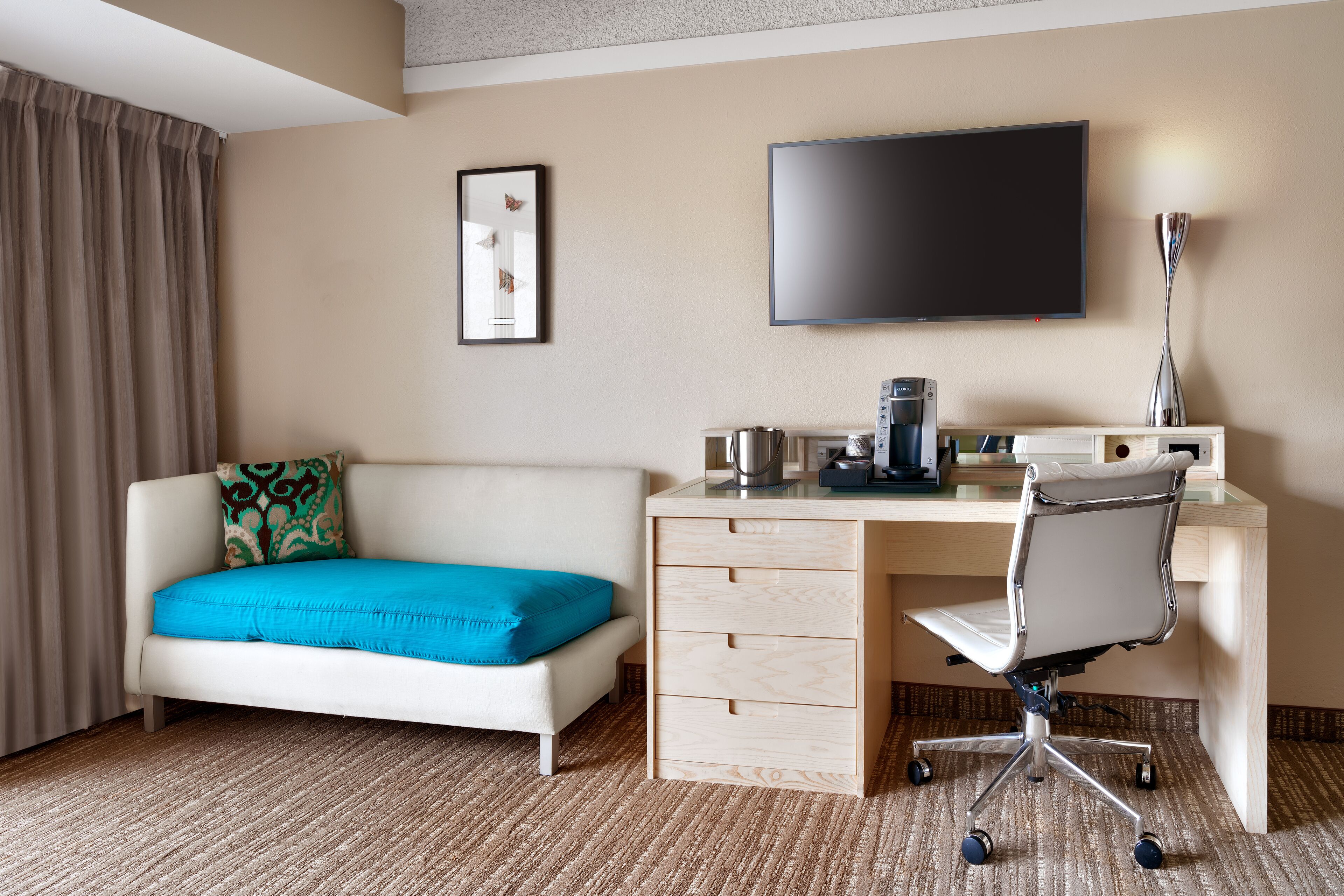 A hotel room with a bed, a desk with a chair, a flat-screen TV, a coffee maker, and a lamp.