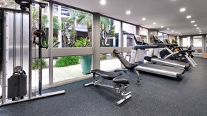 A gym with exercise equipment, large windows, and a view of palm trees. - Atrium Hotel at Orange County Airport (Irvine)