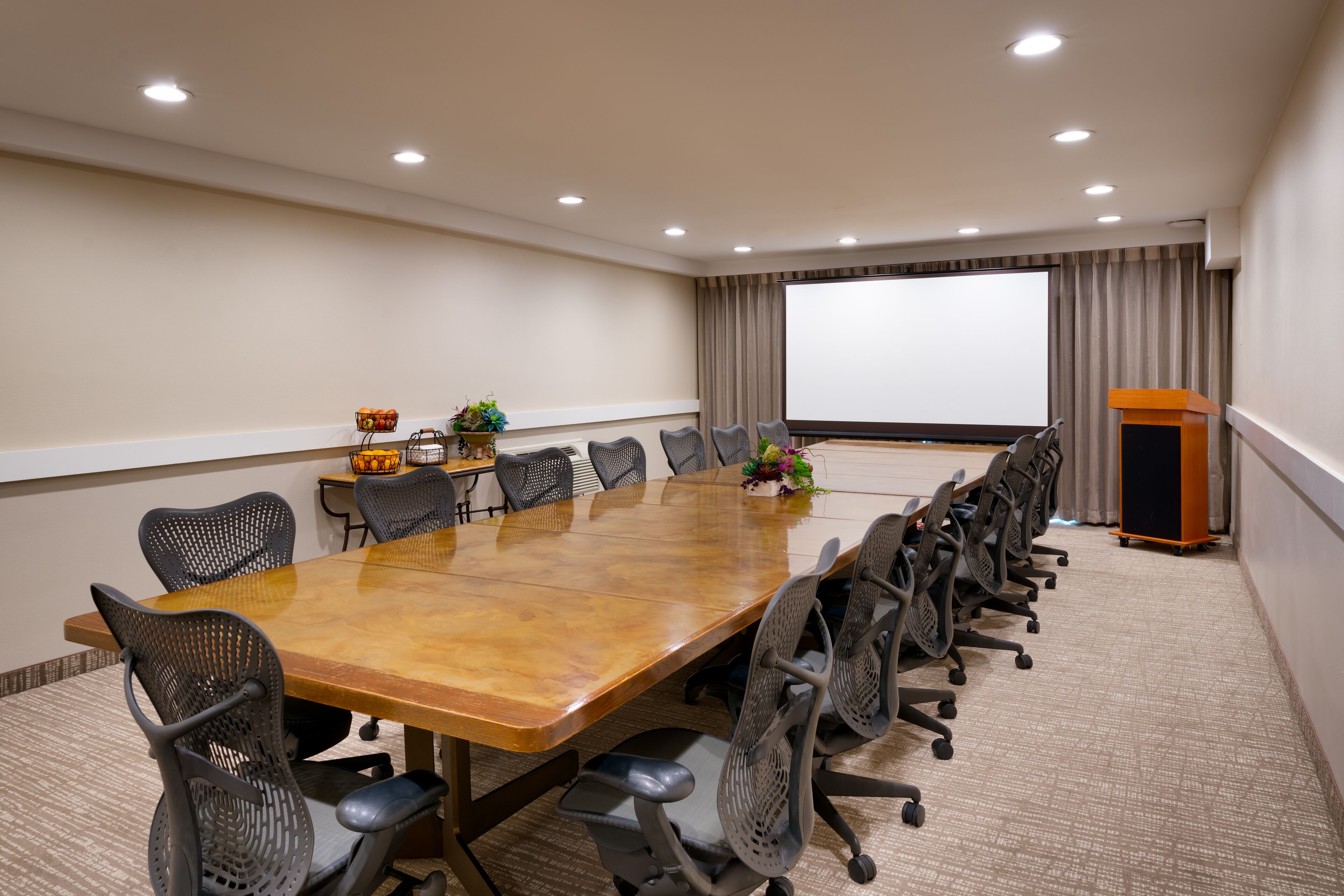 A conference room with a long table, multiple chairs, a podium, and a projector screen.
