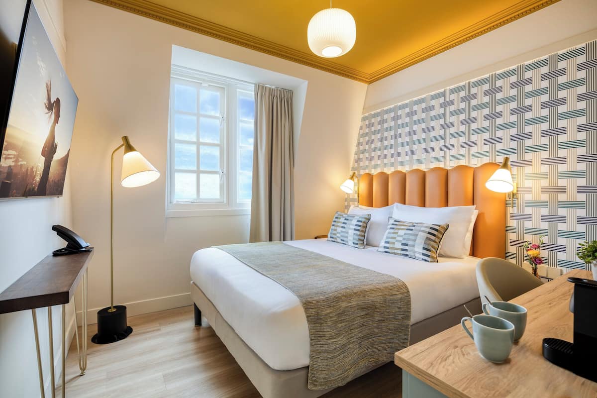 Una camera d'hotel con un letto, due abat-jour, una scrivania, un telefono e carta da parati decorata.