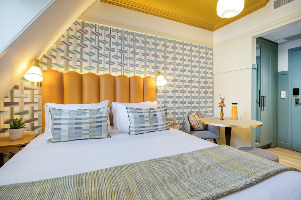 Una camera d'hotel moderna con un letto grande, due abat-jour, un tavolino con un vaso e una parete decorata.