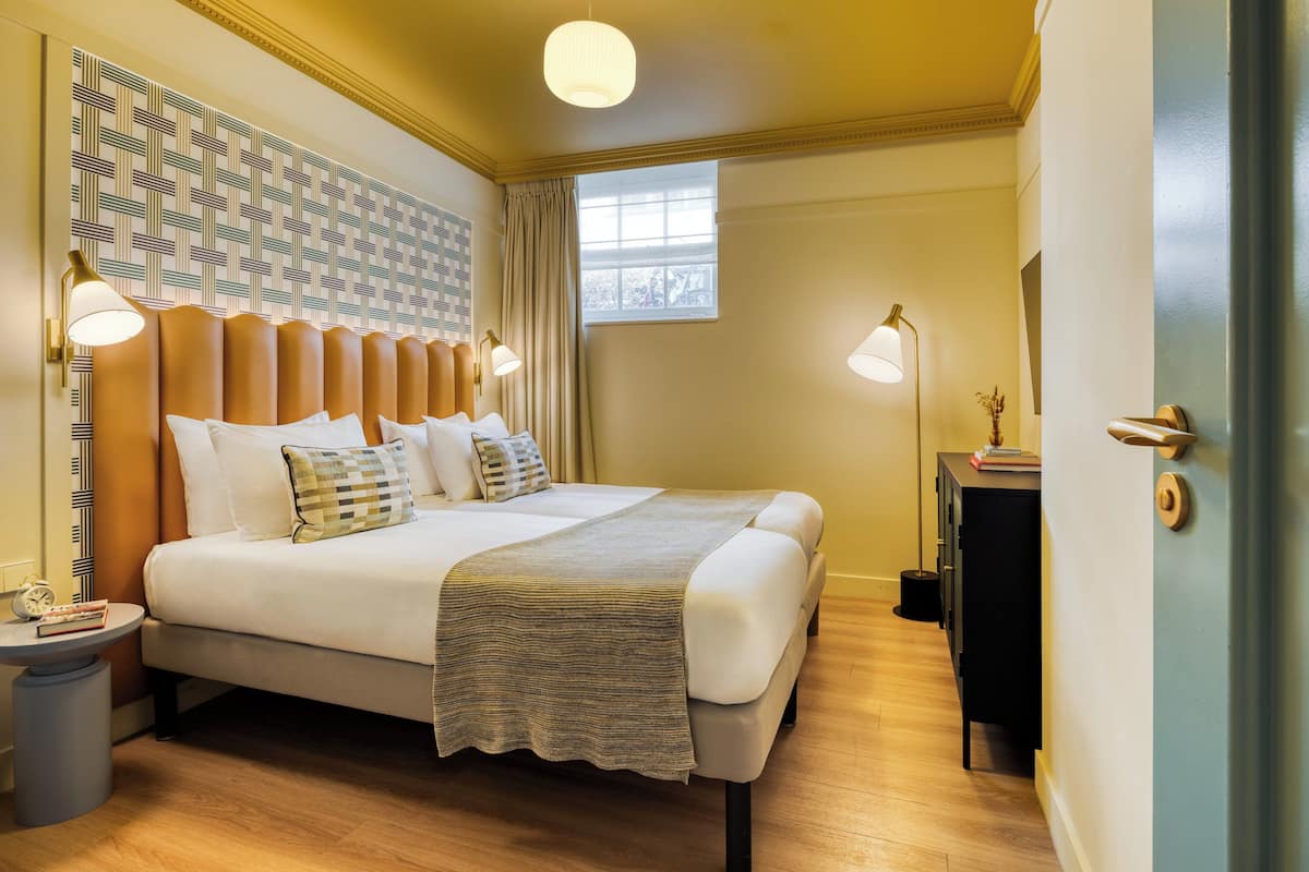 Camera d'albergo con un letto grande, due abat-jour, un comodino, una finestra con tende e una parete decorata.