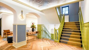 Una habitación amplia con piso de madera en espiga, una escalera verde con barandilla decorativa y un panel ornamental en la pared.