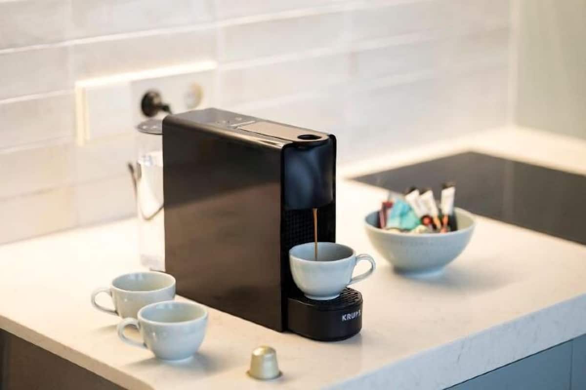 Una moka su un piano di lavoro della cucina, con due tazze bianche e una ciotola con zucchero e cialde per il caffè.