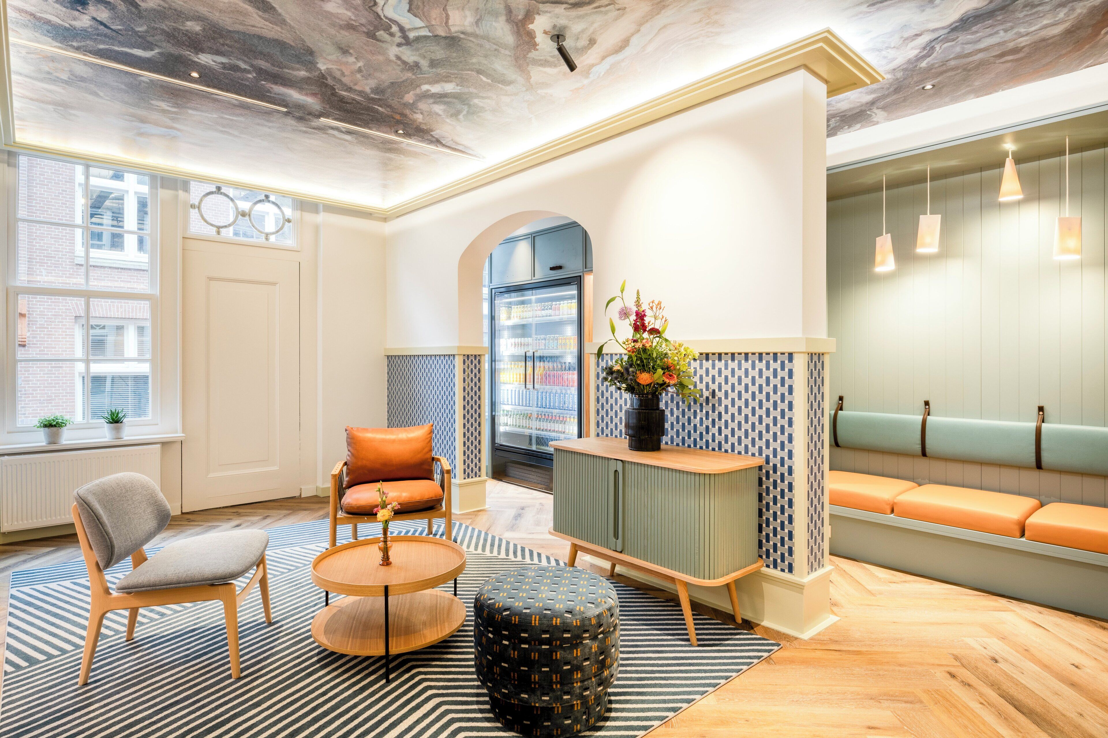 A modern lobby with a seating area, a refrigerator, and a decorative vase.