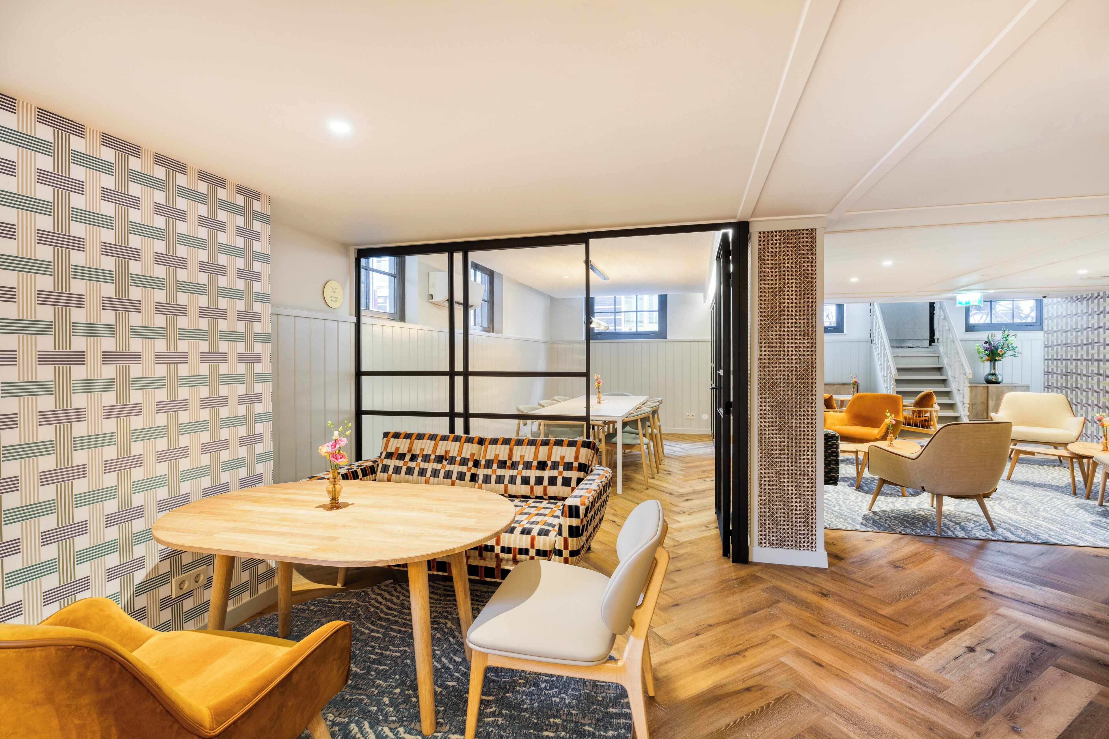 Un interior moderno con una mesa redonda de madera, sofá estampado y un suelo de madera en espiga.