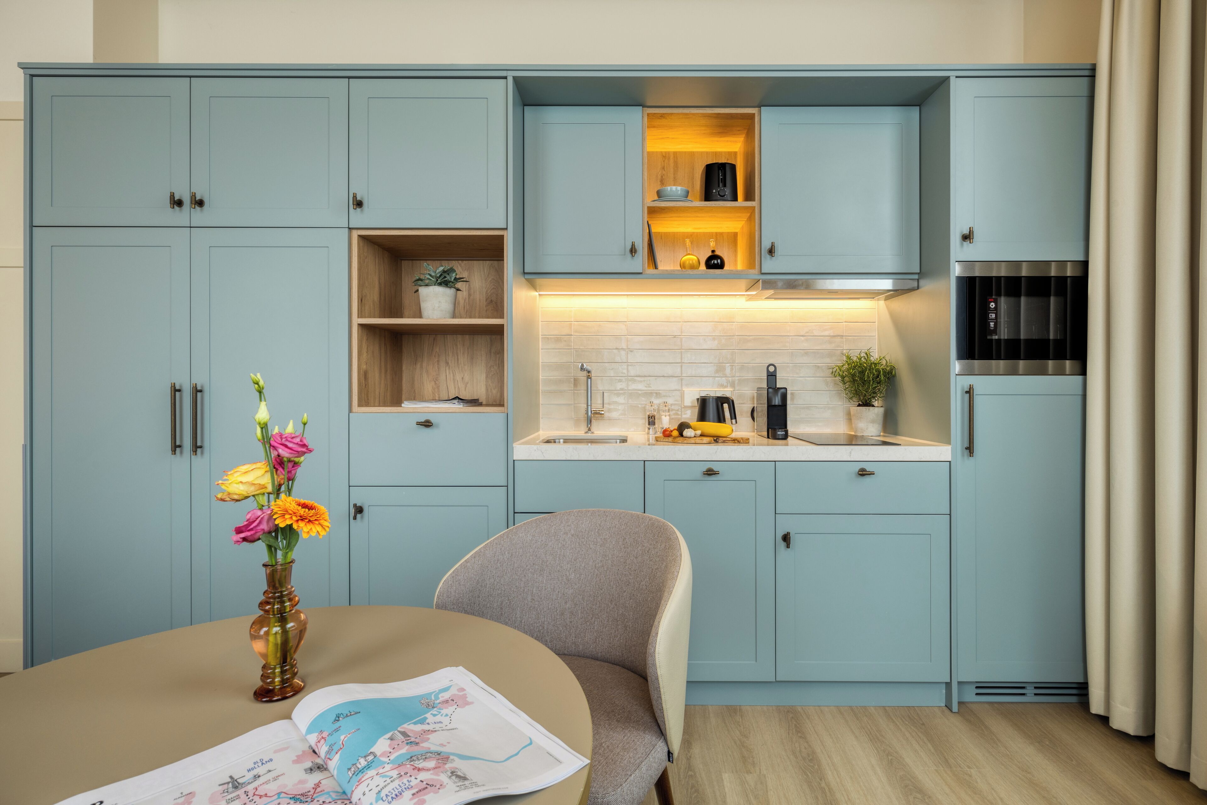 Una cocina moderna con armarios azul claro, una isla central y un comedor con una silla y una mesa.