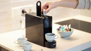 A coffee machine with a cup holder, a bowl with utensils, and two cups on a kitchen counter.
