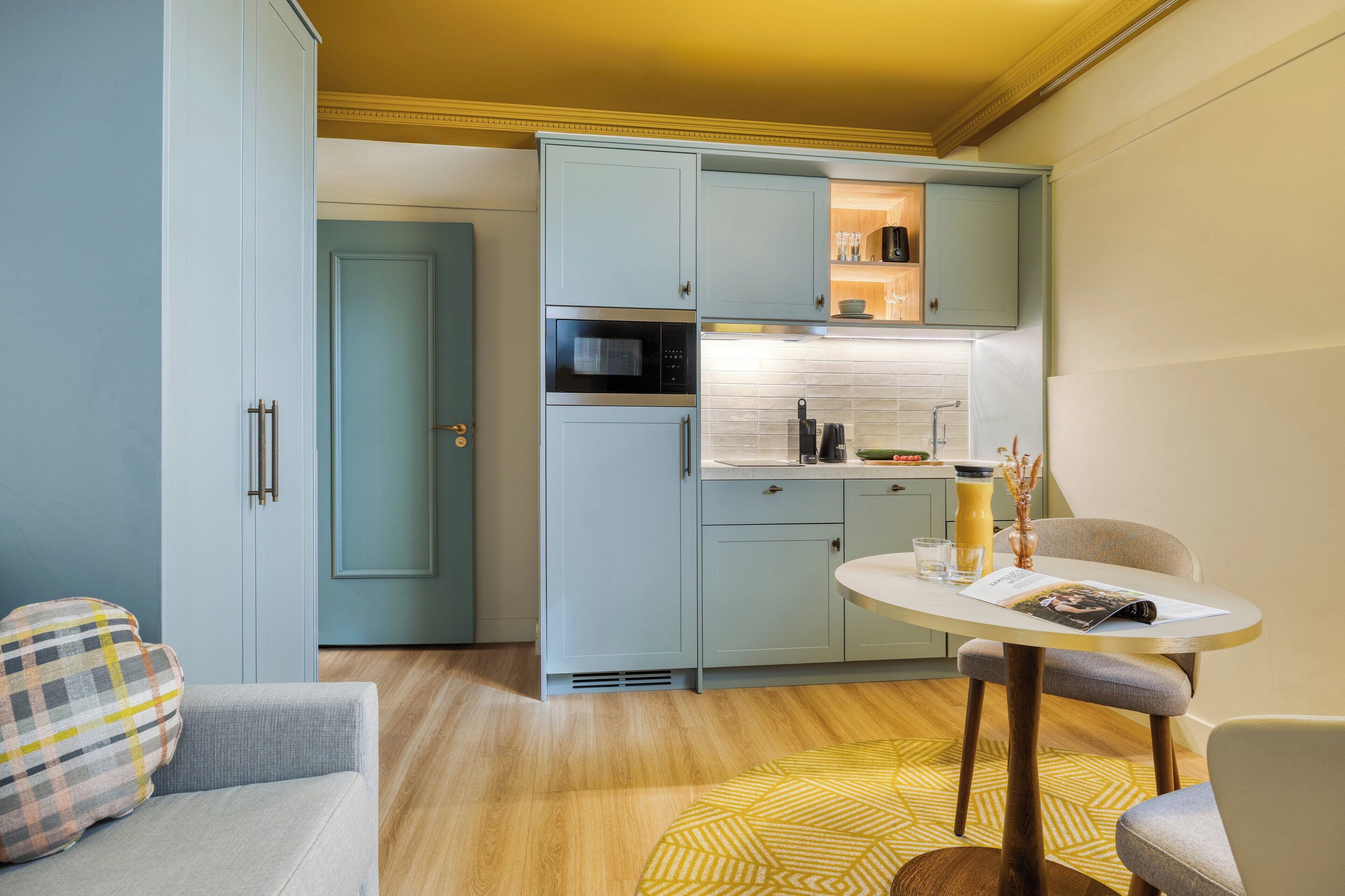 A compact kitchen with light blue cabinets, a microwave, and a small dining area with a table and chairs.