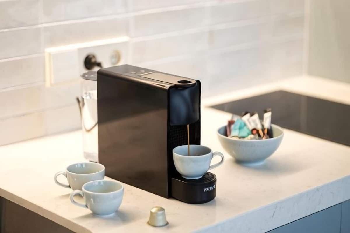 Una moka su un piano di lavoro della cucina, con tazze e una ciotola di zucchero.