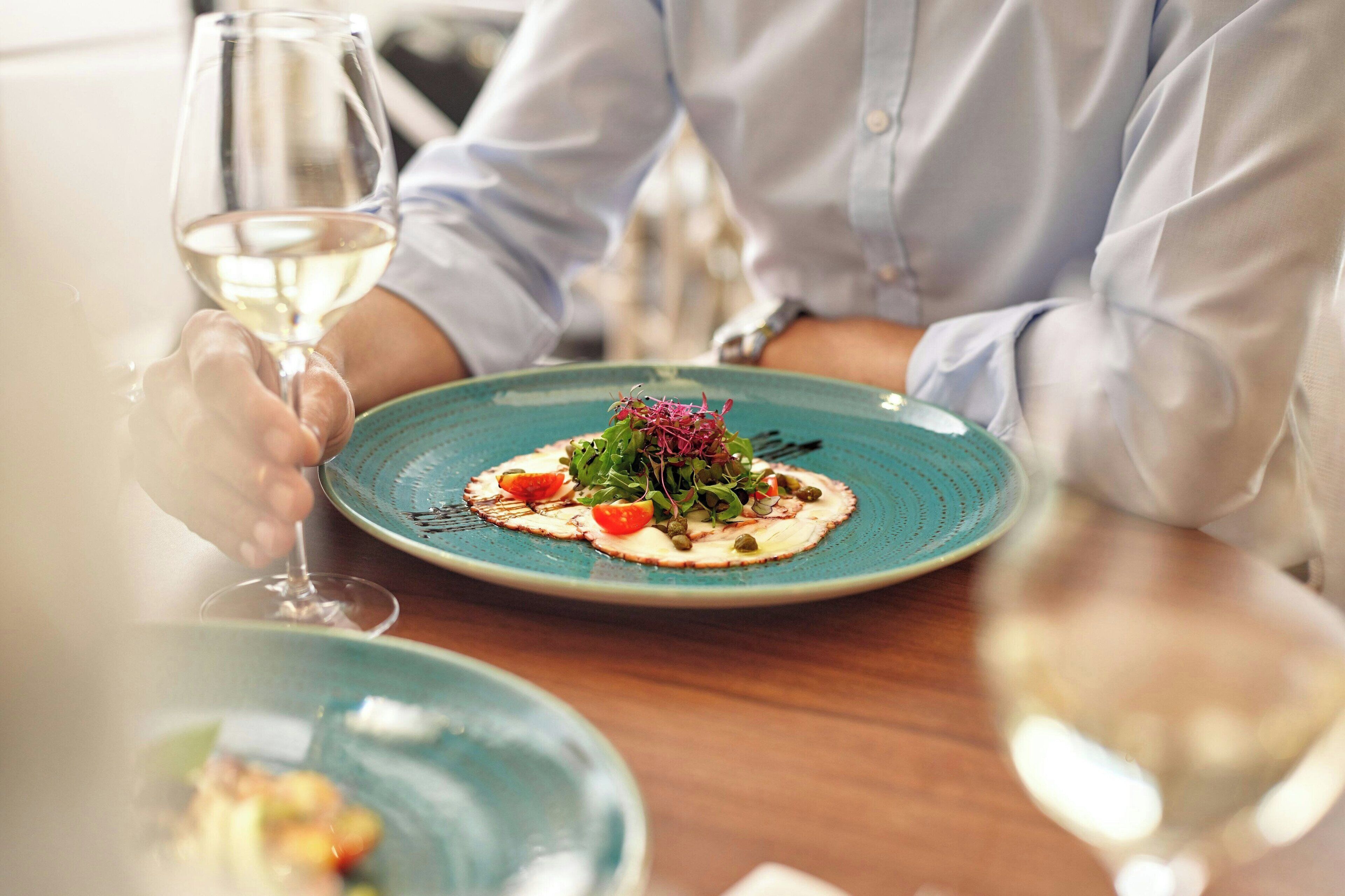 A dining table with a plate of food and a glass of white wine.