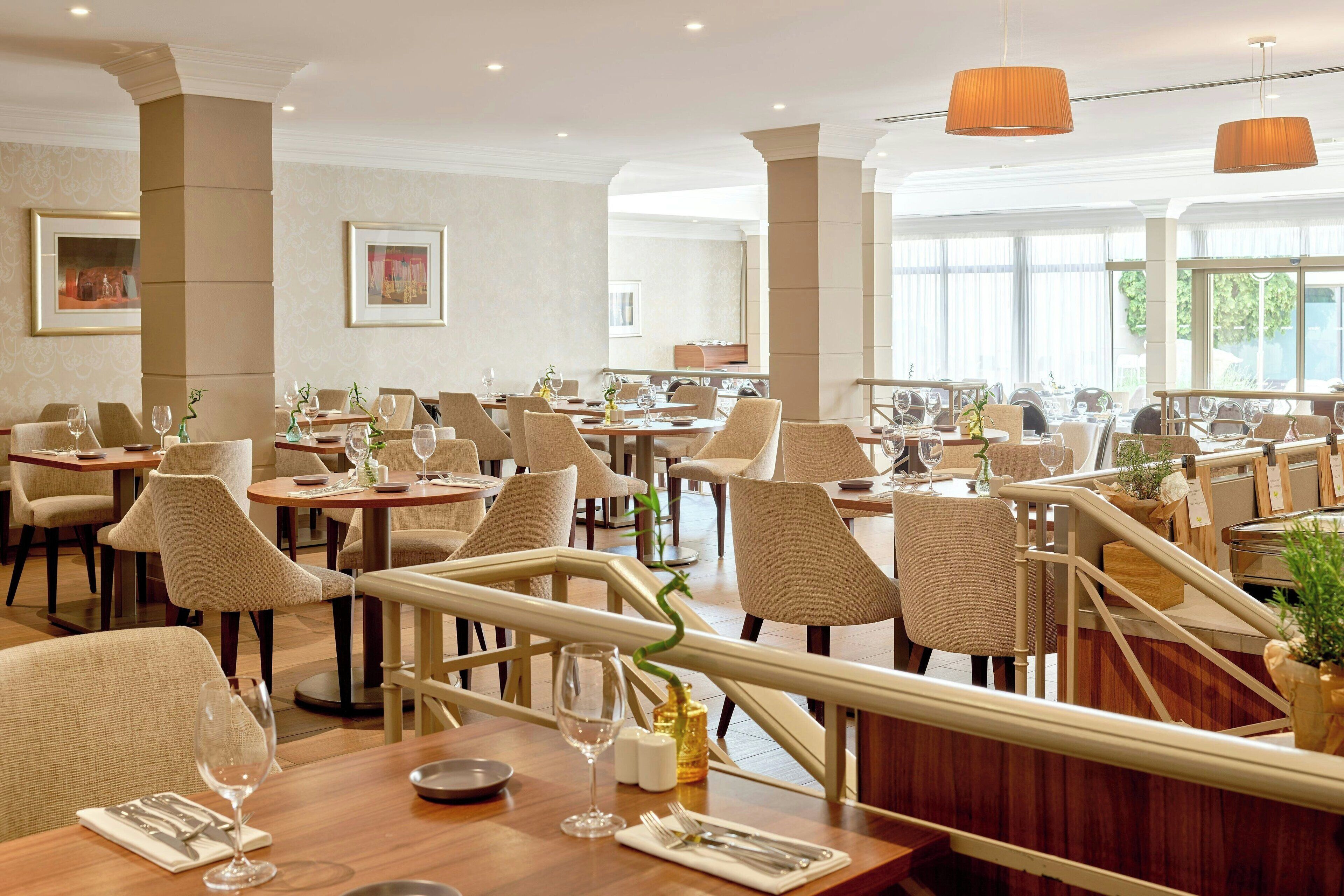 Un restaurante espacioso con múltiples mesas y sillas, ventanas amplias y un diseño interior moderno.