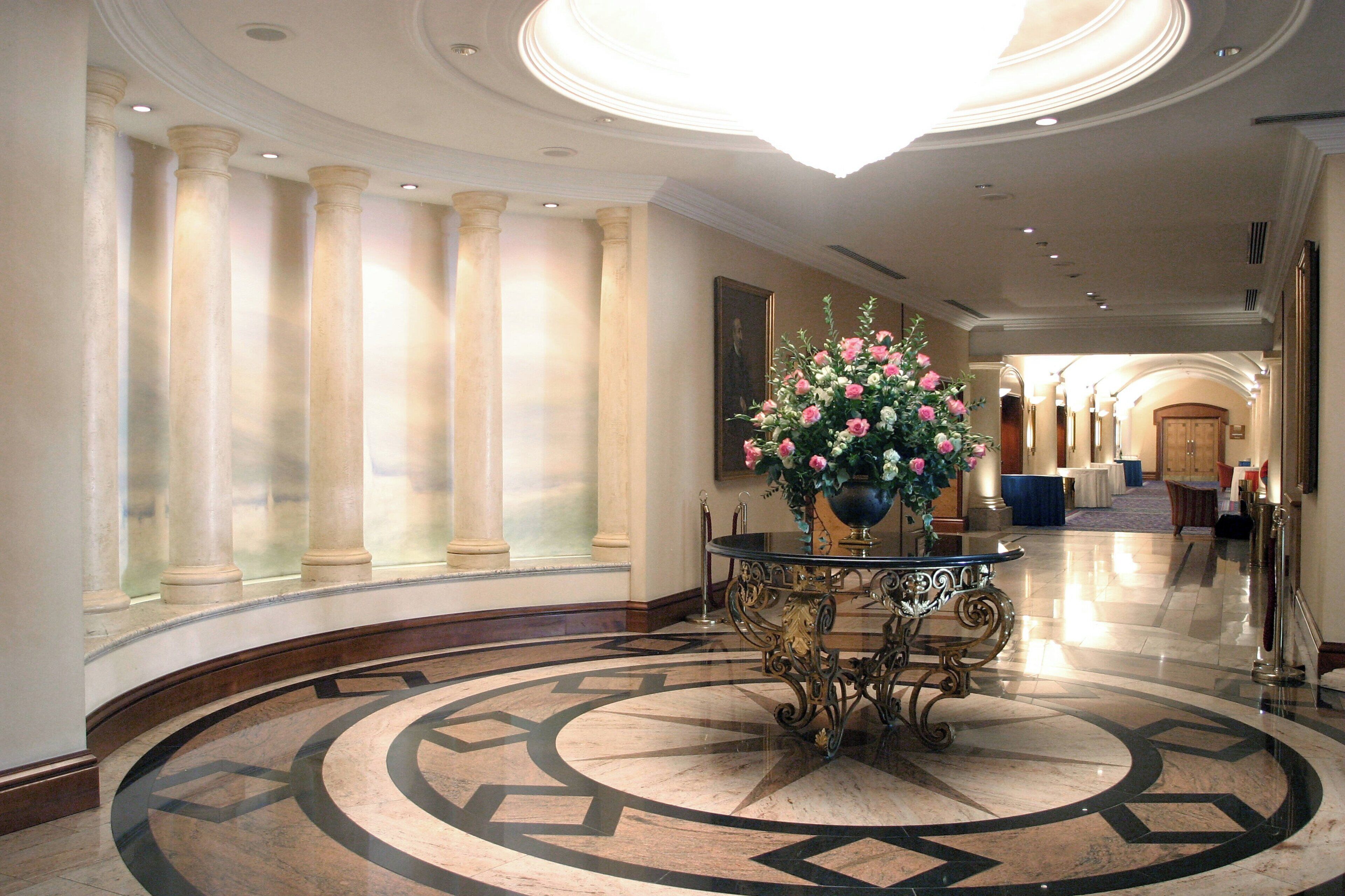 Un lobby espacioso con piso de mármol, columnas y una mesa central con un arreglo floral.
