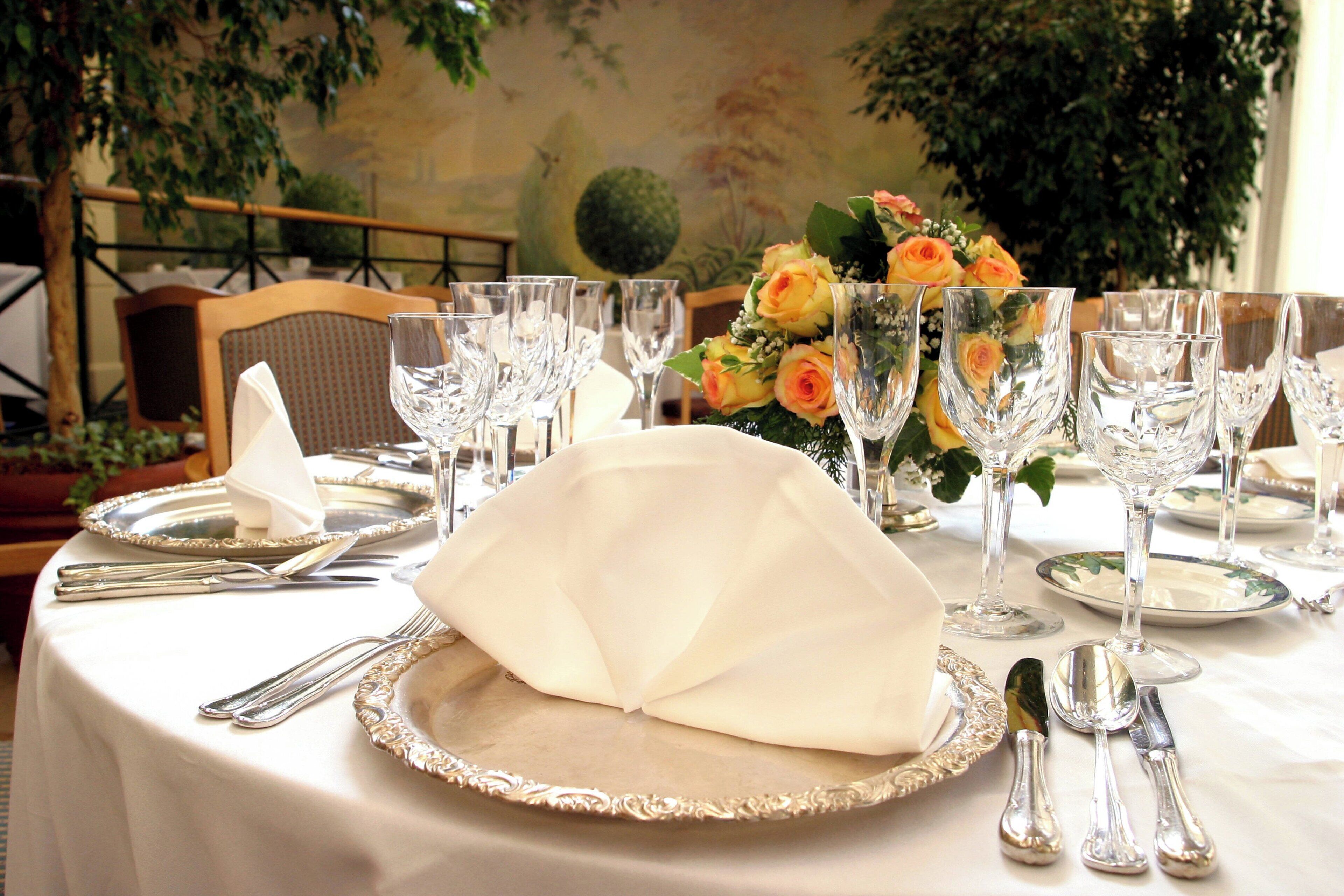 A table set for a formal dining experience with a white tablecloth, silverware, and a centerpiece of yellow roses.