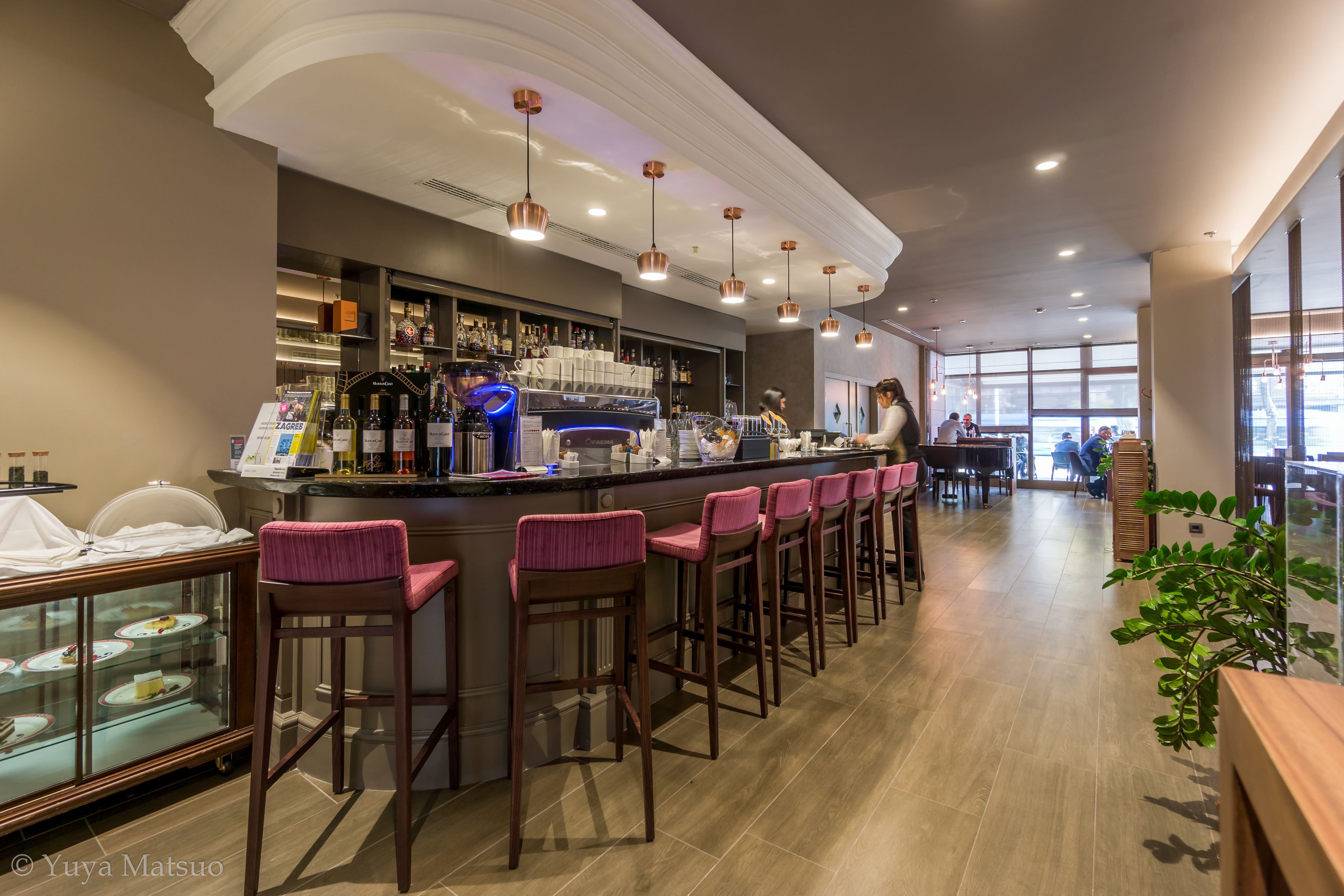 A bar area with a long counter, multiple stools, and a display case with desserts.