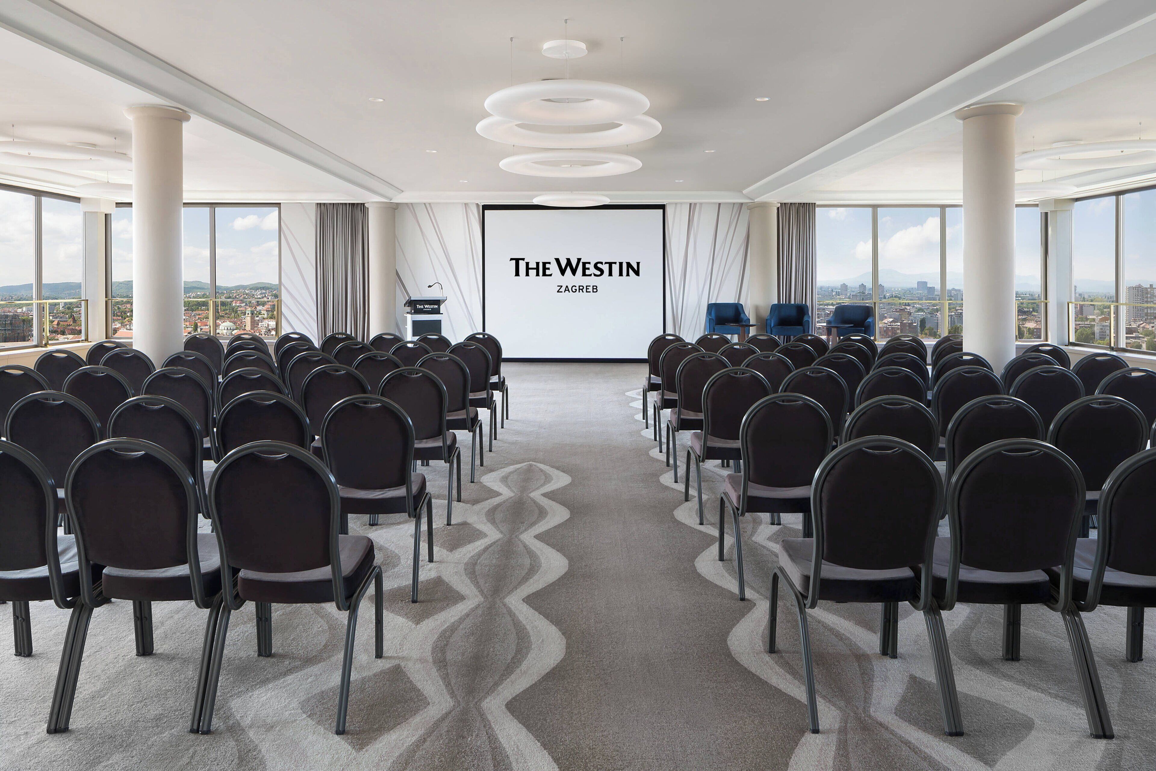 A conference room with rows of chairs facing a large screen displaying "The Westin Zagreb".
