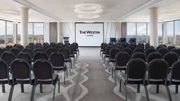 Uma sala de conferências com fileiras de cadeiras voltadas para uma tela grande exibindo 'The Westin Zagreb'.