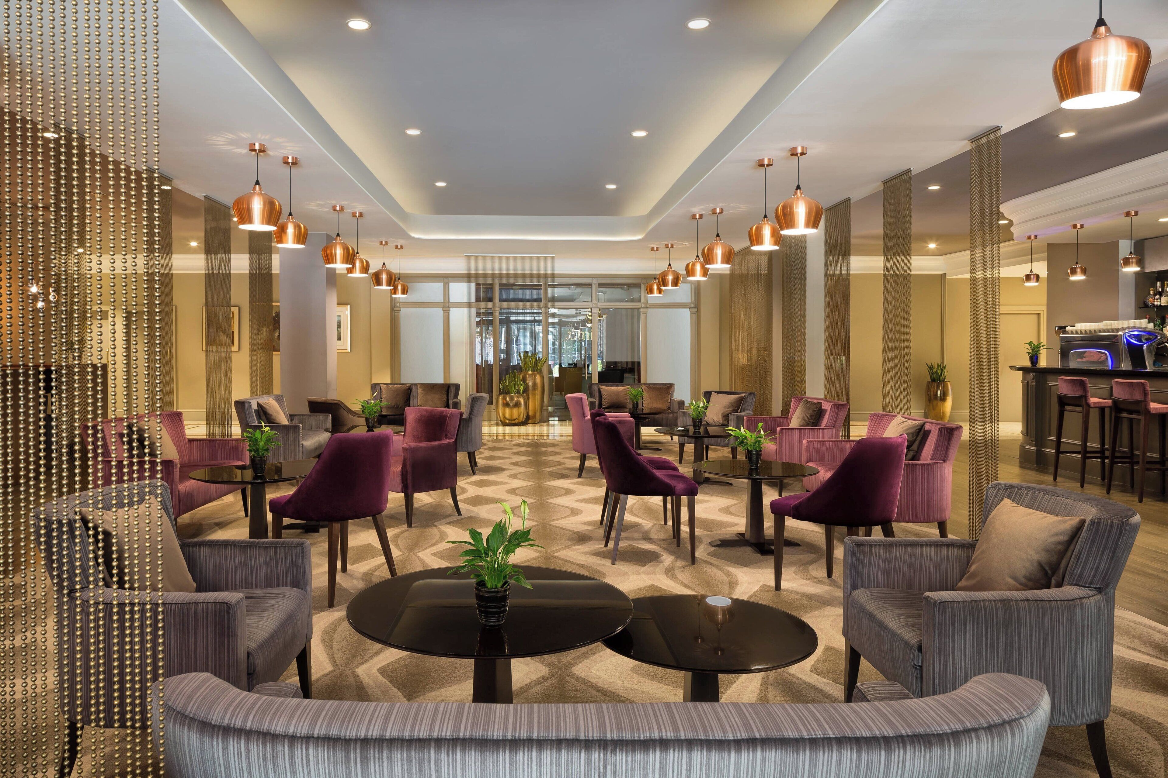 Een ruime lobby met meerdere zithoeken, waaronder banken en stoelen, rond tafels met potplanten.