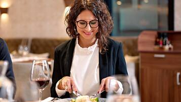 Una persona cenando en una mesa, con una copa de vino y platos de comida.