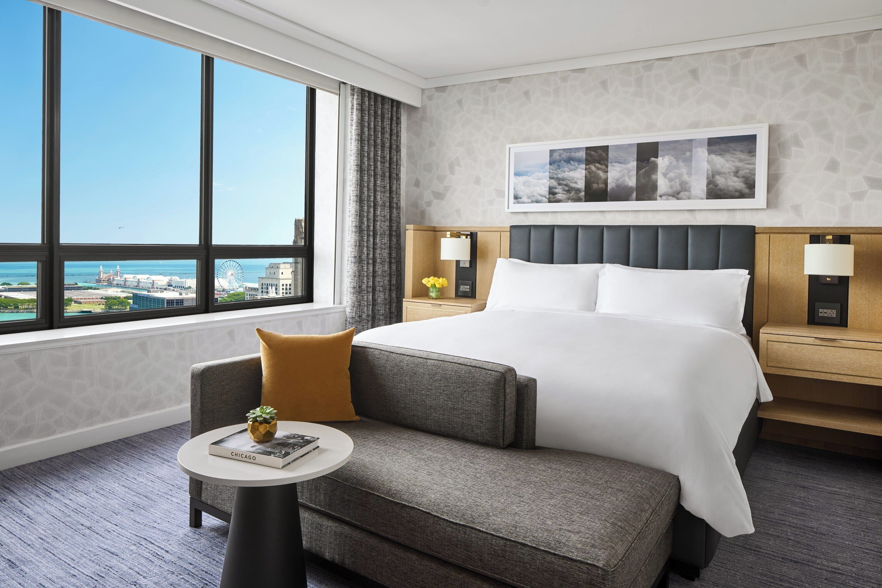 A hotel room with a large window, a bed, a small table, and a nightstand.