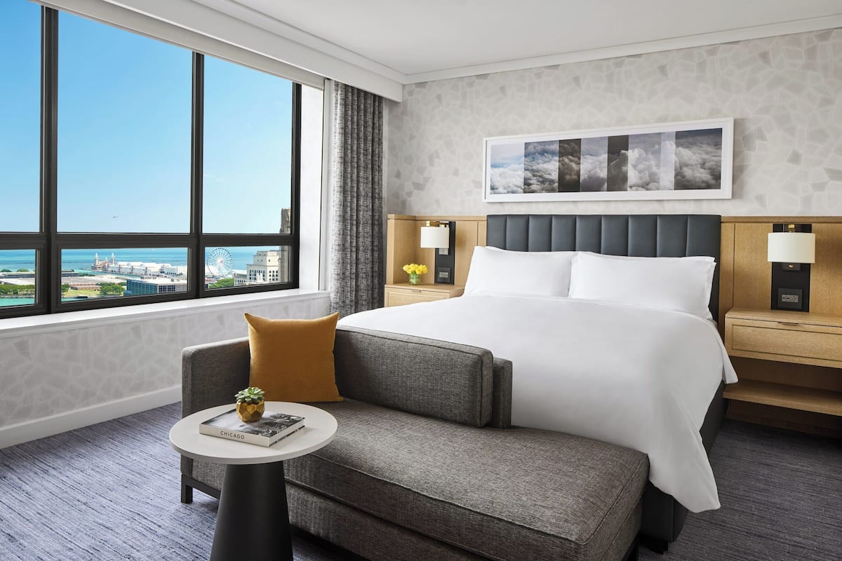 A hotel room with a large window, a bed, a small table, and a nightstand.