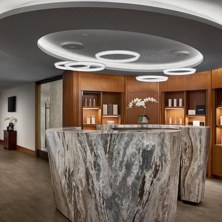 A modern reception area with a marble counter, wooden shelving, and circular ceiling lights.