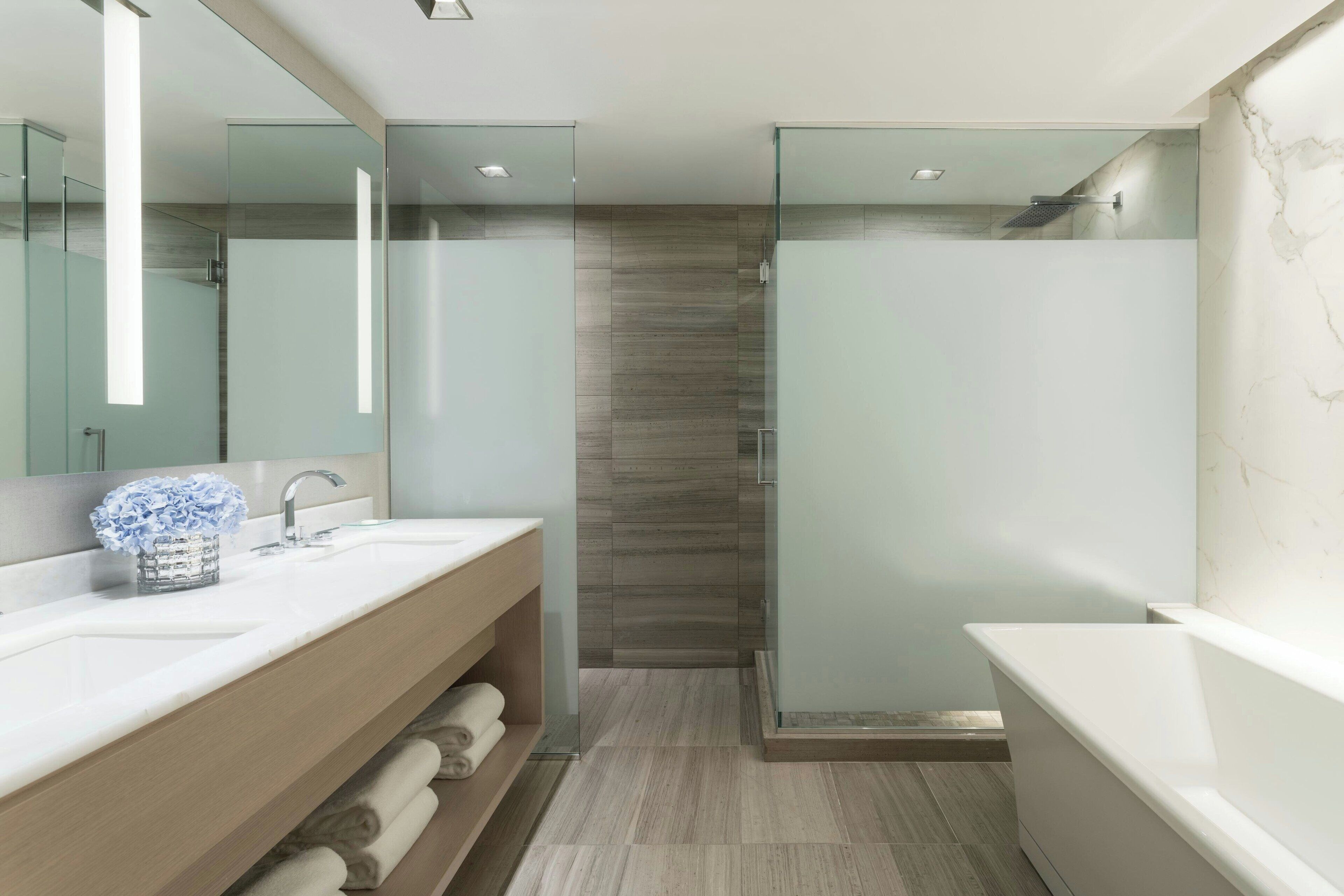 A modern bathroom with a glass-enclosed shower, a large mirror, and a wooden vanity with a sink.