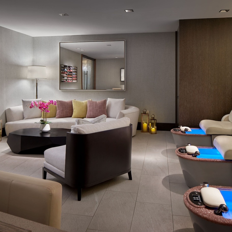 A modern spa room with a sofa, armchairs, a massage table, and a wall-mounted mirror.