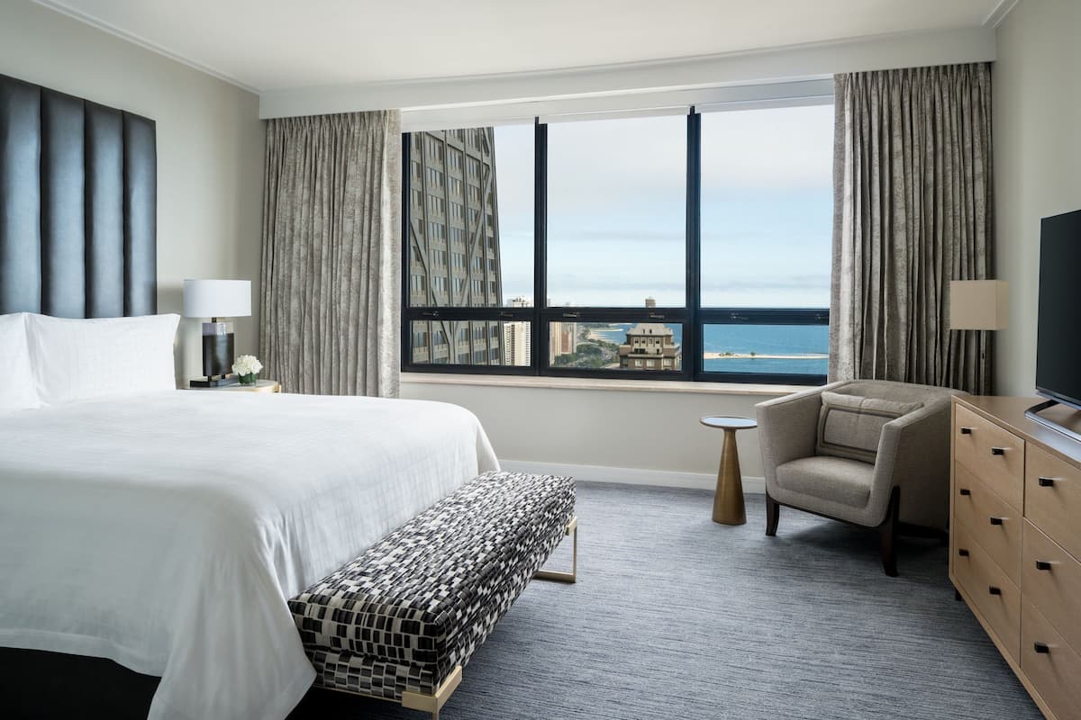 A hotel room with a large bed, a view of the sea, a chair, and a TV.