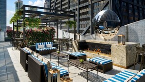 A rooftop lounge with outdoor seating, a fire pit, and a large reflective sculpture.