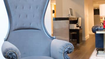 Un sillón tapizado y elegante con detalles ornamentales, ubicado en una habitación moderna con piso de madera y una paleta de colores neutros.