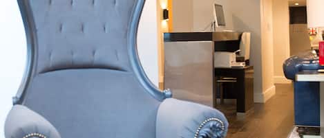 Un sillón tapizado y elegante con detalles ornamentales, ubicado en una habitación moderna con piso de madera y una paleta de colores neutros.